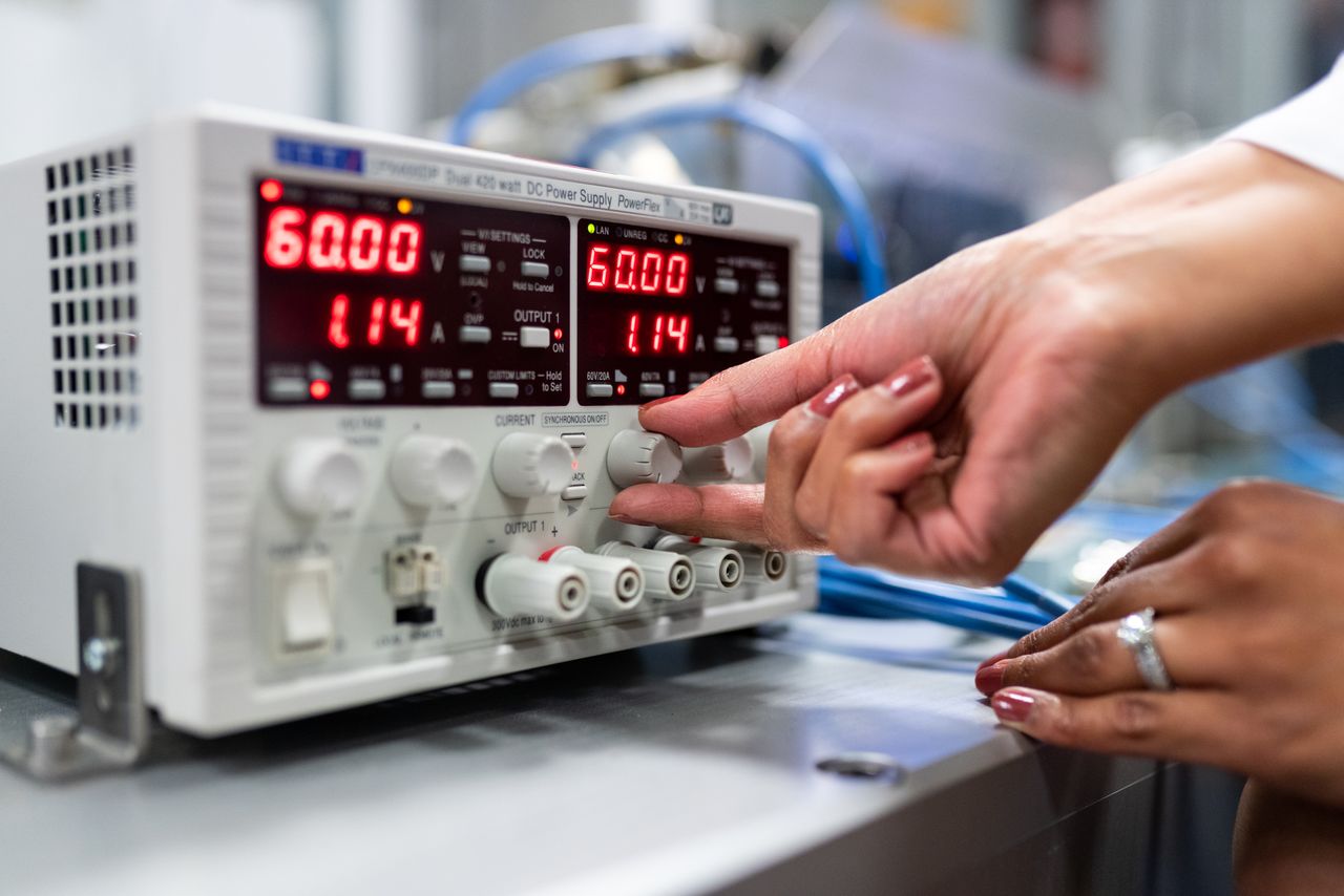 Hands adjusting dials on laboratory DC power supply.